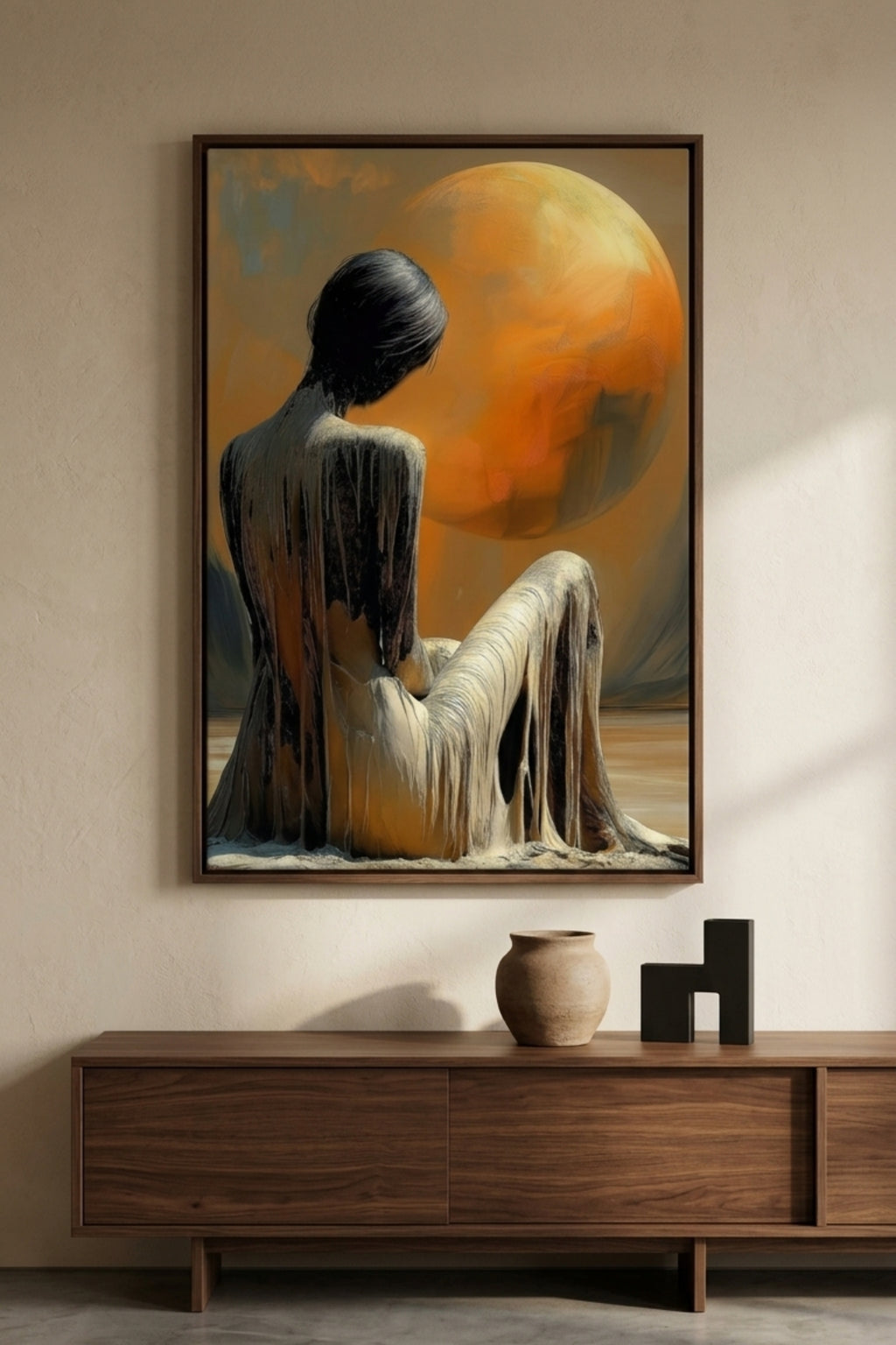 Framed artwork of a woman sitting with a large orange moon on a wall above a wooden console table.